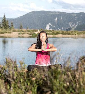 Dunkelhaarige Frau macht Yoga am See